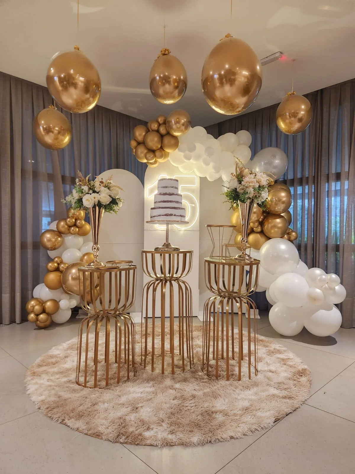 Decoração elegante em dourado e branco com balões suspensos pela Decoreba Festas